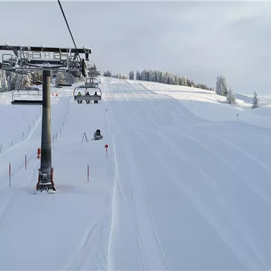 A ski slope with fresh snow and a cable car in the foreground. The trees are covered in snow and the sky is slightly cloudy.