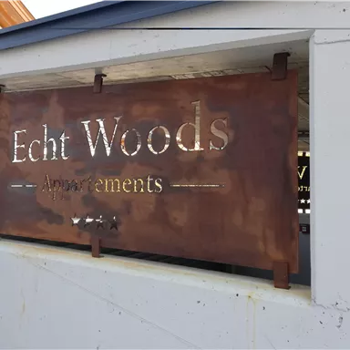 The image shows a sign with the inscription "Echt Woods" and the word "Announcements". The sign is made of metal and has a rustic appearance.