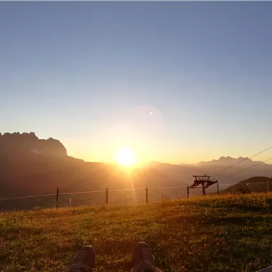 A beautiful sunset over the mountains. The landscape is peaceful with grassy areas and rocks in the background.