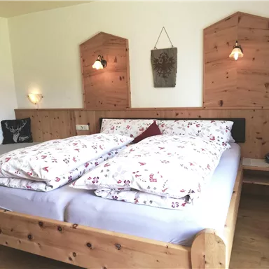 Ein gemütliches Schlafzimmer mit einem Holzbett und schöner Bettwäsche. Die Wände sind aus Holz, und es gibt sanftes Licht von den Wandlampen.