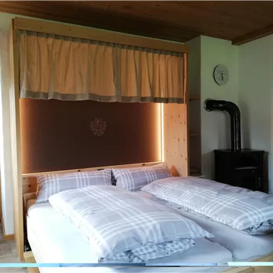 Ein gemütliches Schlafzimmer mit einem großen Bett und karierten Bettdecken. Die Wände sind aus Holz und es gibt einen kleinen Ofen.