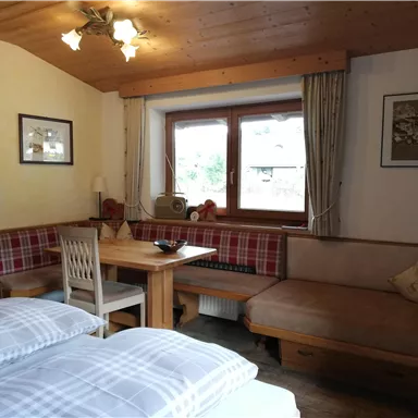 Ein gemütlicher Innenraum mit einem Tisch und Sitzgelegenheiten. Es gibt große Fenster, die viel Tageslicht hereinlassen.