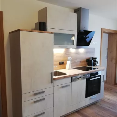 Eine moderne Küche mit hellen Schränken und einer eleganten Arbeitsplatte. Sie ist mit Geräten wie einem Herd und einer Kaffeemaschine ausgestattet.