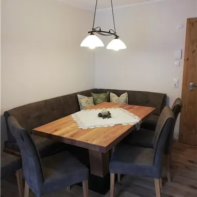 Ein gemütlicher Essbereich mit einer Holztafel und einer Eckbank. Die Stühle sind grau und eine attraktive Lampe hängt über dem Tisch.