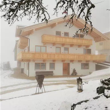 Ein gemütliches Haus mit Holzbalustraden, umgeben von Schnee und Nebel. Die winterliche Landschaft vermittelt eine ruhige und friedliche Atmosphäre.