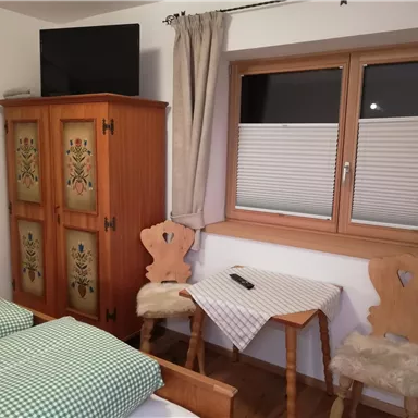 Ein gemütliches Zimmer mit zwei Betten und einem Holzschrank. Am Fenster stehen ein Tisch und zwei Stühle.