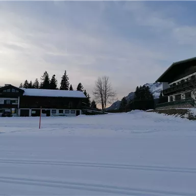 A winter landscape with snow-covered buildings. In the background, trees and mountains can be seen.