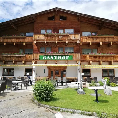 A traditional inn in alpine style with an inviting outdoor area.  
In front of the building are tables and chairs for relaxing outdoors.