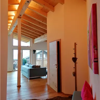 A modern hallway with high ceilings and wood paneling. On the left side, there is a couch and a table, while on the right side, there is a wardrobe.