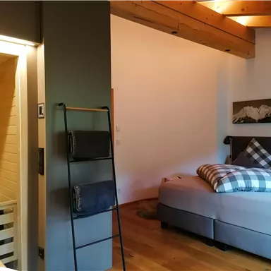 A modern room with a wooden beam ceiling and a cozy bed. On the left is a sauna inviting you to relax.