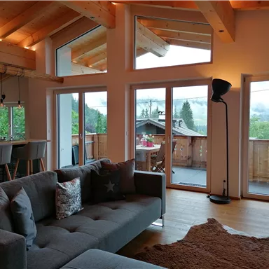 A modern living room with a cozy sofa and large windows. The view of nature in the background enhances the inviting atmosphere.