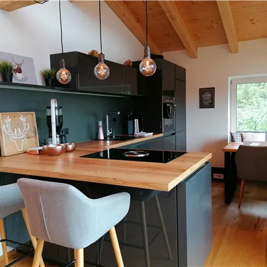 A modern kitchen with a wooden countertop and stylish bar stools. Large windows provide plenty of daylight and a cozy atmosphere.