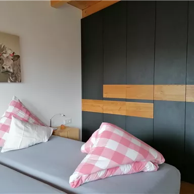A cozy bedroom with a bed and checkered pillows. The wall is designed in dark tones with wooden accents.