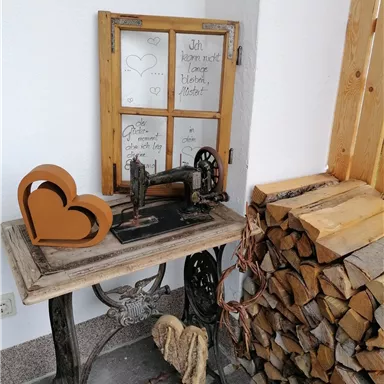 An old sewing machine on a table next to a stack of wood. In the background, there is a window with handwritten notes.