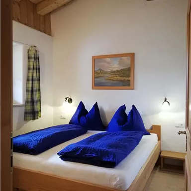A comfortable bedroom with a double bed and blue pillows. The wooden walls and the roof structure give a rustic charm.