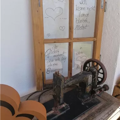 An old sewing machine is on a table next to a heart-shaped decorative object. In the background, there are labeled windows with romantic messages.
