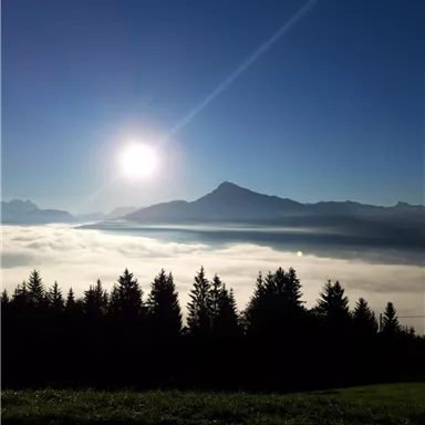 An impressive mountain landscape with low-hanging clouds and radiant sunlight. The sky is clear and blue.