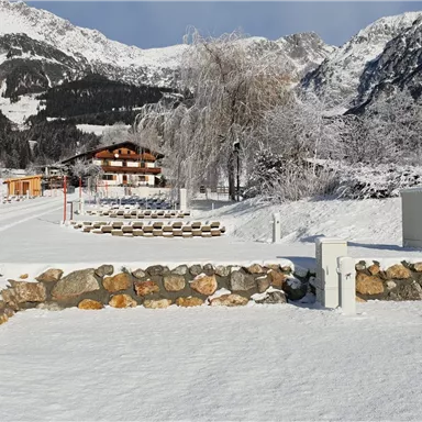 Eine winterliche Landschaft mit schneebedeckten Bergen und einem ruhigen Bauernhaus. Der Boden ist mit frischem Schnee bedeckt, und die Umgebung wirkt friedlich und idyllisch.