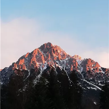 A majestic mountain with a snow-capped peak. The sky is clear and the sun illuminates the rocks in warm colors.