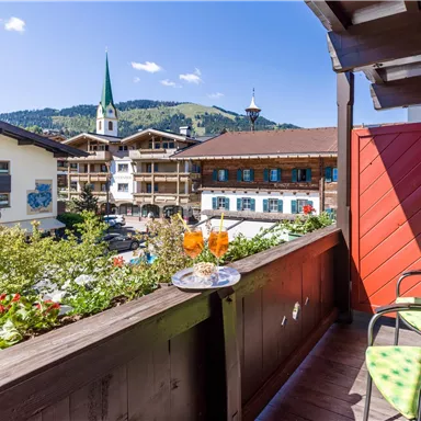 A beautiful balcony overlooking a charming town.
Two drinks and snacks are on a table, while the mountains are visible in the background.