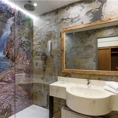 A modern bathroom with a glass shower and a large mirror. The walls are decorated with a beautiful nature motif depicting a waterfall.