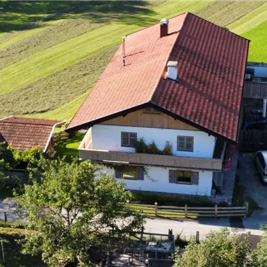 Ein traditionelles Haus mit roten Dach in ländlicher Umgebung. Blick auf einen gepflegten Garten und parkende Autos.