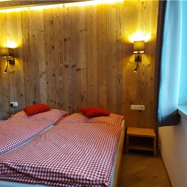 Ein gemütliches Zimmer mit zwei Einzelbetten und karierten Bettwäsche. Die Wände sind aus Holz und es gibt sanfte Beleuchtung.