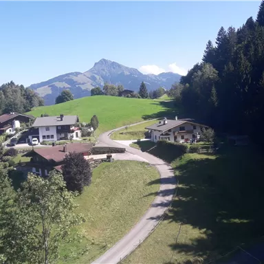 A picturesque landscape with typical Alpine houses and gentle hills. In the background, a majestic mountain rises under a clear sky.