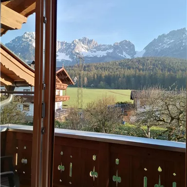 Ein Blick auf die Alpenlandschaft mit schneebedeckten Bergen und einem schönen grünen Tal. Die Aussicht wird von einem Balkon aus genossen.