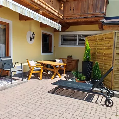 A cozy outdoor area with a seating corner and a sunshade. The terrace is surrounded by a wooden fence and plants.