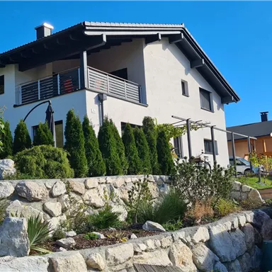 Ein modernes Haus mit einer schönen Fassade und einem Garten. Die Umgebung ist grün und gepflegt, mit einer Steinmauer im Vordergrund.
