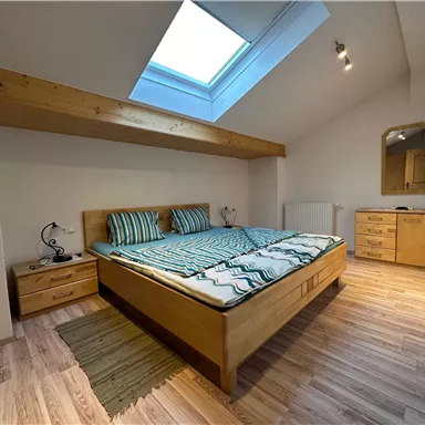 A cozy bedroom with a double bed and wooden furniture. The room has a window with daylight and a modern look.