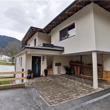 A modern house with a driveway and a parking space. In the background, hills and a cloudy sky are visible.