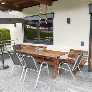 An inviting outdoor area with a wooden table and chairs. A sunshade protects against direct sunlight.