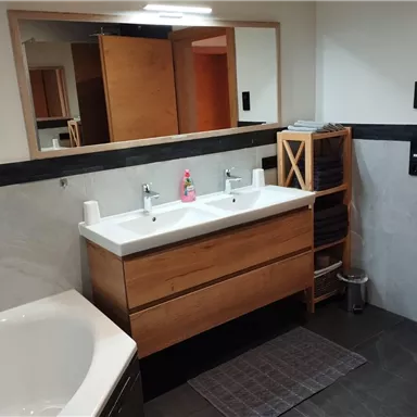 A modern bathroom with a double sink made of wood and elegant fixtures. The walls are light and the floor is made of dark tiles.