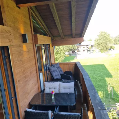 A beautiful balcony with a table and chairs made of rattan. In the background, you can see a green meadow and trees.
