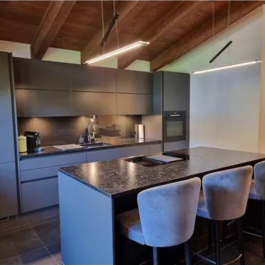 Modern kitchen with a large kitchen island and stylish bar stools. The room has a bright and open atmosphere with wooden ceilings and modern surfaces.