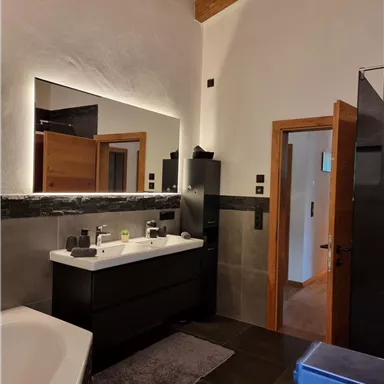 A modern bathroom with a wooden ceiling and elegant furnishings. There is a large sink, a bathtub, and a shower.