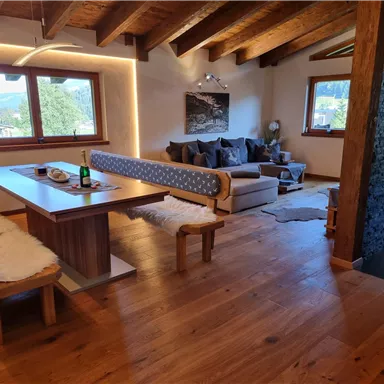 A cozy living kitchen with wooden ceilings and a large dining area. In the background, there is an inviting sitting area with a view of the countryside.