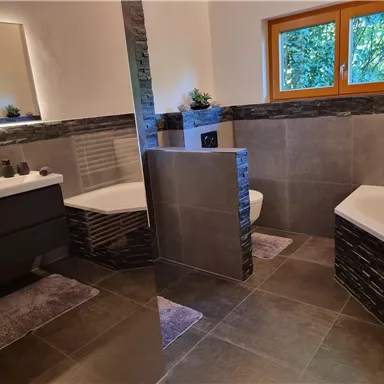 A modern bathroom with an elegant bathtub and a stylish sink. Large windows let in plenty of daylight and offer a view of the green surroundings.