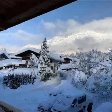 Two rows of snow-covered houses under a clear blue sky. Majestic mountains can be seen in the background.