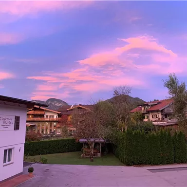 A picturesque landscape with gentle hills and a beautiful, colorful sky. In the foreground stands a residential house with a well-maintained garden.