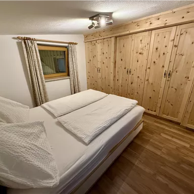 A cozy bedroom with a double bed and wooden wardrobes. Large windows provide light and a bright atmosphere.