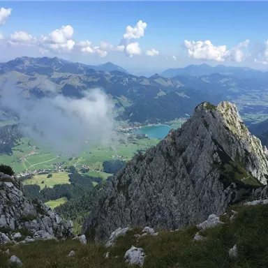 Ein atemberaubender Blick auf die Berge mit grünen Tälern und einem klaren See. Die Wolken ziehen sanft über die Landschaft.