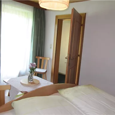 A bright room with a bed, a table, and chairs. The window lets in a lot of light and creates an inviting atmosphere.