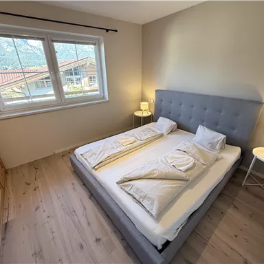 A cozy bedroom with a double bed and bright walls. Large windows offer a view of the surroundings.