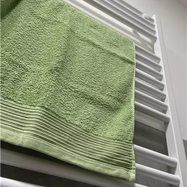 A green towel is lying on a white towel rack. The background is bright and modernly designed.