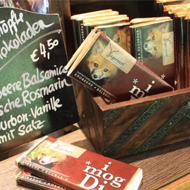 A rustic wooden stand with various chocolate bars. Next to the chocolates is a board with the price and the offered flavors.
