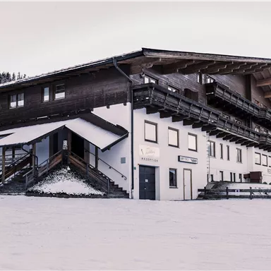 A cozy building in the snow with a classic alpine design. Surrounded by snow-covered trees and mountains.
