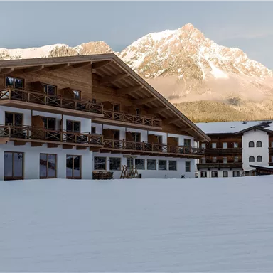 A cozy hotel in the snow with a view of the mountains. The facade is made of wood and features balconies overlooking the winter landscape.